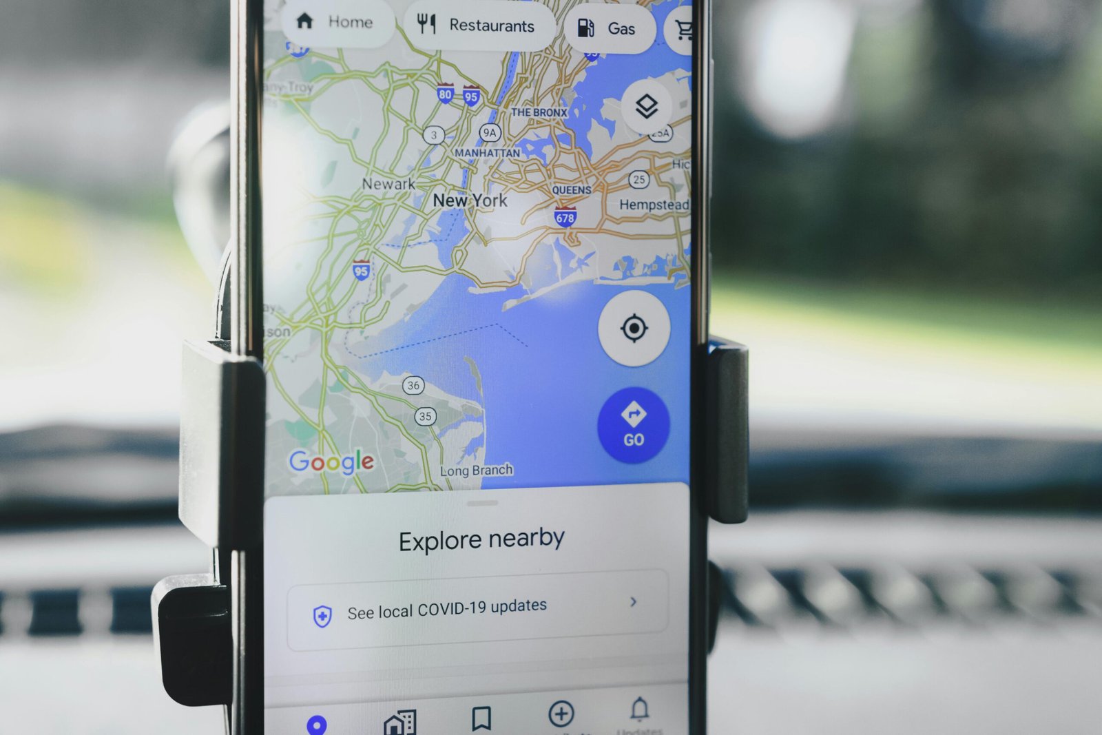 A smartphone displaying GPS map of New York City secured in a car mount during daylight.